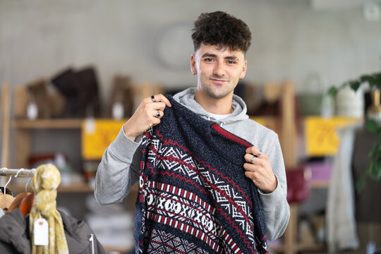 Regular guy client pre-examine fabric and style of product, is busy choosing sweater. Client enjoys shopping for clothes at store browsing through colorful on display racks