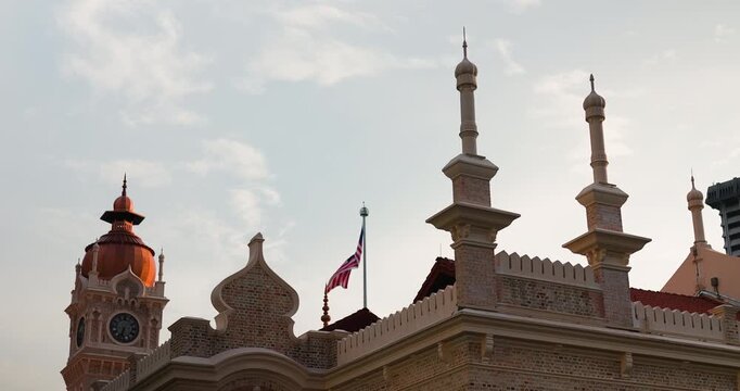 The Majestic Sultan Abdul Samad Building in Kuala Lumpur, Malaysia, Featuring its Iconic Clock Tower and the Malaysian Flag Waving Against a Cloudy Sky