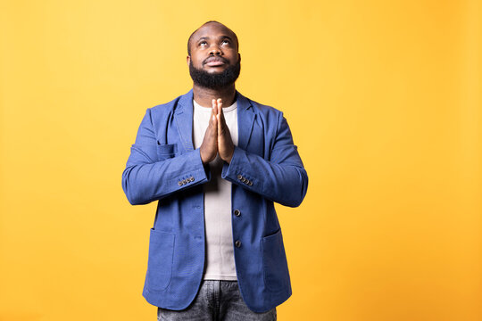 Pious African American man praying to his god, asking for forgiveness, spiritual BIPOC man doing worship hand gesturing, confessing, begging for pardon, isolated over studio background.