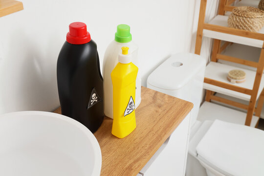 Household cleaning products with skull and crossbones warning labels in a modern bathroom setting