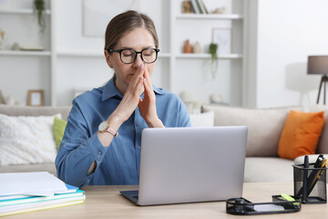 Fototapeta premium Workaholic. Overwhelmed woman in glasses at wooden desk with laptop and stationery indoors