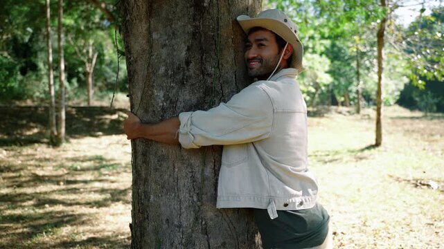 Smiling man embracing a large tree trunk in a natural forest environment. Concept of environmental conservation, sustainability, ecological awareness, biodiversity protection, and human connection wit