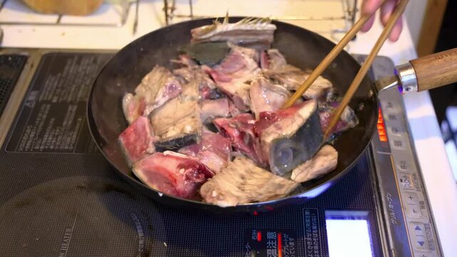 鰤アラのオリーブ煮を調理中、鰤のアラを霜降りで鉄フライパンで焼き、菜箸で裏返しするシーン