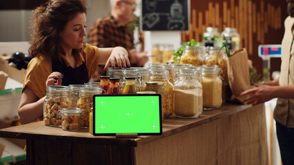 Customers shop next to chroma key tablet with copy space used as commercial sign in zero waste shop. Promotional ad on green screen device in food store with products in reusable decomposable package.
