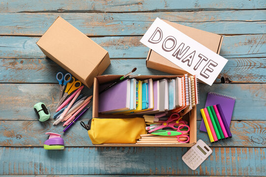School supplies donation box with stationery and "donate" sign on rustic wooden background