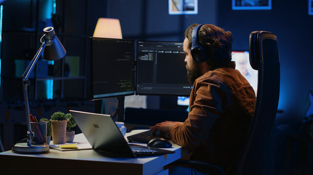 Engineer typing code in apartment office, using javascript programming language to develop software application. IT admin using multimonitor desktop setup and notebook to finish tasks, camera A.