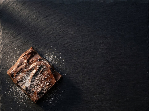 Chocolate brownie with sugar dusting on dark slate stone background