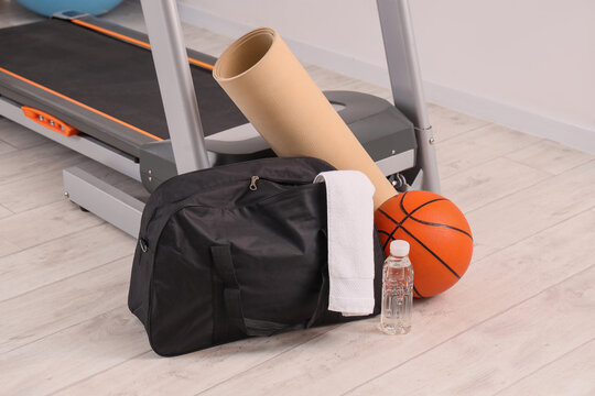 Home gym fitness equipment with treadmill, yoga mat, duffle bag, basketball, towel, and water bottle for workout