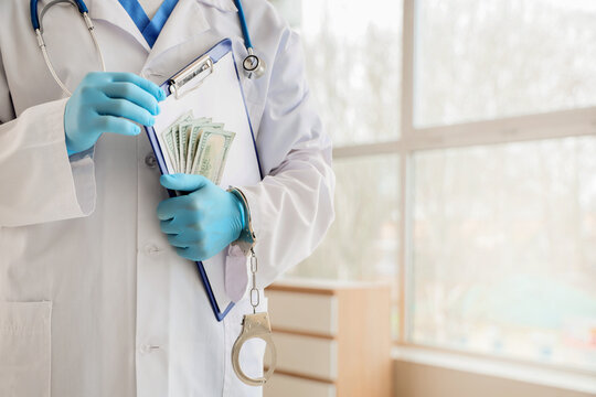 Medical corruption and healthcare fraud, doctor in white coat with stethoscope holding money and clipboard, handcuffed for bribery