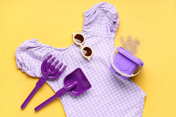 Obraz premium Childrens summer beach vacation essentials purple gingham swimsuit sunglasses sand toys and bucket on yellow background
