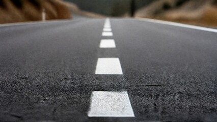 Fototapeta premium White dashed lines on asphalt road, minimalist perspective with natural daylight and shallow focus.