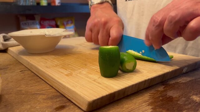 Man chopping fresh green jalapeno pepper on wooden cutting board