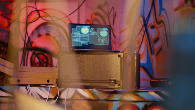 Laptop in underground bunker with graffiti painted walls left behind by hackers to act as decoy, running script pinging wrong location to cybercriminal law enforcement chasing them.
