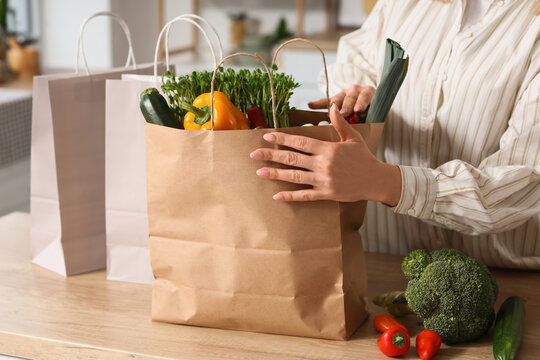 Woman unpacking fresh organic groceries from brown paper bag on kitchen counter, healthy eating and sustainable lifestyle