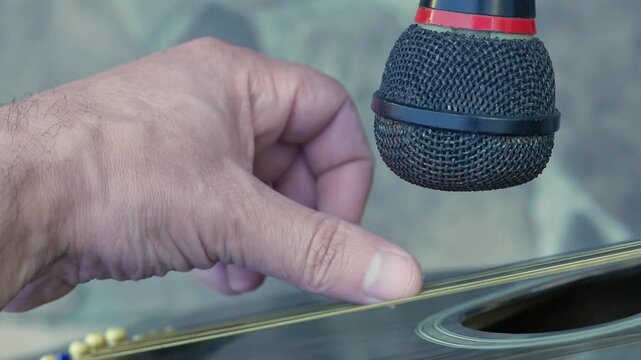 POV (close-up): musician playing acoustic guitar in front of a microphone. A guitarist strumming a guitar. A singer in front of a microphone. An artist plucking a guitar. A man playing guitar. Music. 
