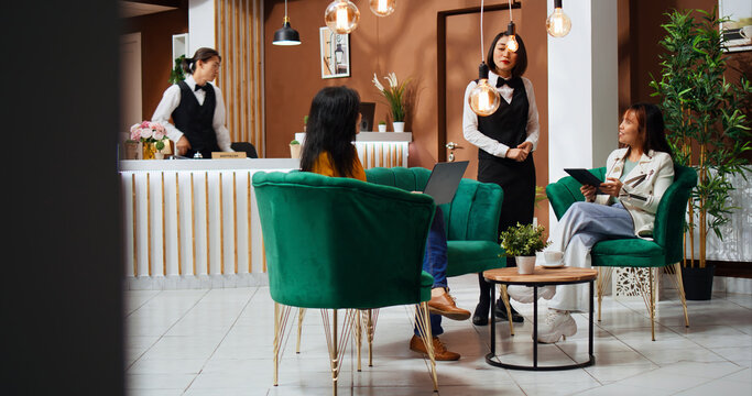 Receptionist providing concierge services for guests in lobby, staff presenting all leisure facilities to ensure pleasant relaxing stay. Asian women asking employee about famous landmarks to visit.