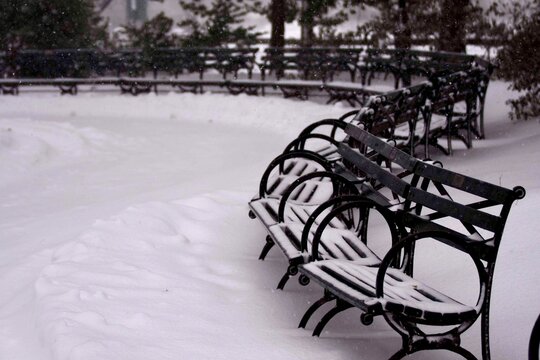 Row of empty park benches covered in deep white snow during winter in New York, USA
