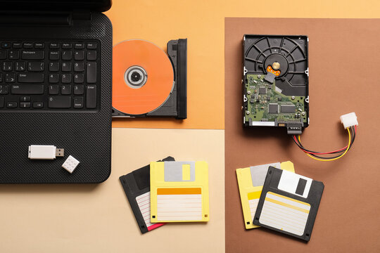 Digital data storage evolution: laptop, USB drive, CD-ROM, hard drive, and floppy disks on color block background
