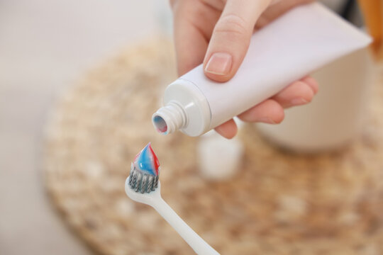 Hand squeezing toothpaste tube onto toothbrush for daily oral hygiene and dental care routine, a hand squeezes a white toothpaste tube, dispensing red and blue striped toothpaste onto the bristles