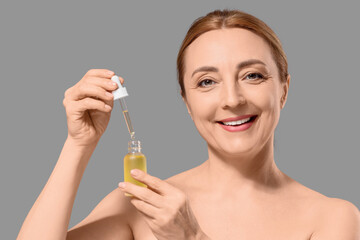 Fototapeta premium Smiling mature woman applying anti-aging facial serum for skincare routine and youthful radiance, the product is in a small bottle with a dropper, cosmetic treatment and self-care