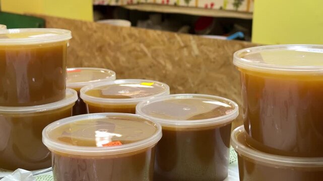 Close-up honey jars on counter warm amber honey in clear plastic containers stacked on cloth market display glossy texture visible