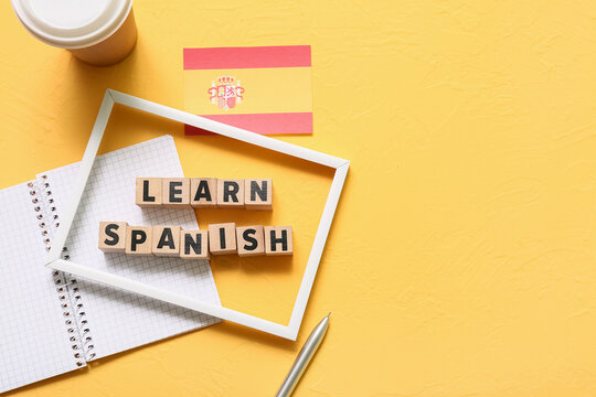 Learn spanish language education with wooden blocks, spanish flag, notebook, and pen on yellow background