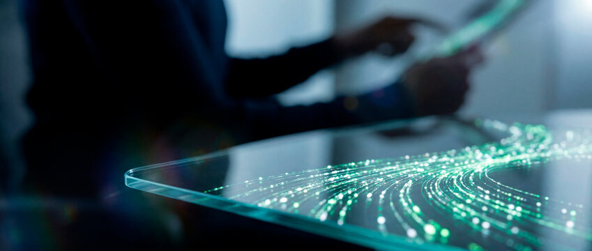 Person using tablet beside glass surface with green fiber optic data streams