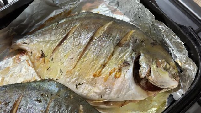 Oven roasted pompano on black platter two golden sea fish scored and roasted in foil top view showing crispy skin browned edges