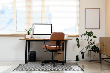 Fototapeta premium Modern home office workspace with blank computer screen, ergonomic chair, and indoor plants for remote work setup