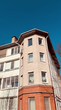 White brick apartment against blue sky. Sunlit multistorey facade with rows of windows, balconies and chimney framed by bare