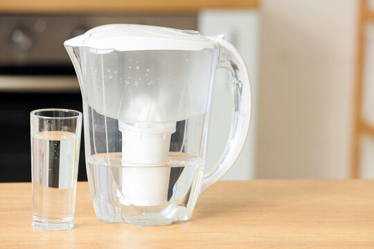 Water filter pitcher and glass of clean drinking water on kitchen countertop for healthy hydration, the transparent pitcher contains a filter cartridge, providing purified water for daily consumption