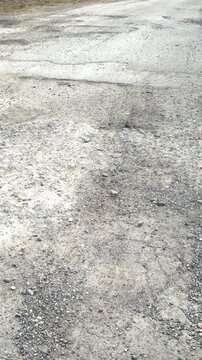 Gravel road pothole damage daytime closeup of rutted asphalt and scattered rubble showing cracked surface texture, uneven patches