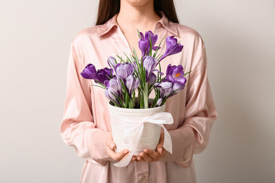 Woman in pink silk blouse holding white potted purple crocus flowers with ribbon, springtime gift and floral decoration, the pot is adorned with a delicate white ribbon