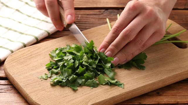 Woman cutting fresh parsley at wooden table, closeup