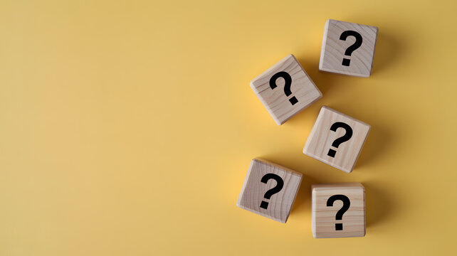 Wooden blocks with question marks arranged on a minimalist yellow background for creative problem solving concepts and conceptual thinking strategy ideas representing uncertainty