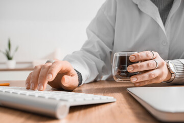 Fototapeta premium Young female doctor with cup of coffee and computer working at table in hospital, closeup
