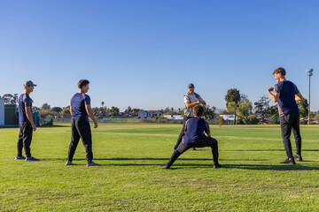 Obraz premium Male team practicing on cricket pitch, bowler holding cricket ball, keeper crouching near stumps
