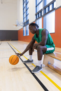 Orange basketball bouncing on polished hardwood court near wooden bench with green jersey and hoop