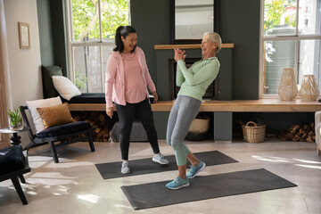 Obraz premium Diverse female trainer guiding senior woman balancing on dark mats in living room activewear