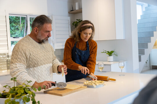 Couple preparing filled pastries at home kitchen island, cutting dough with pastry wheel
