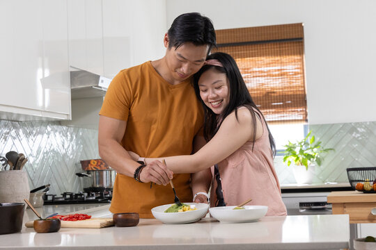 Asian couple preparing food on kitchen island with white bowls wearing orange tee and pink headband