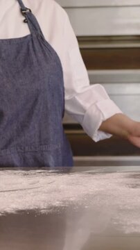 Vertical video: Pinching flour from bowl chef apron dusting, spreading steel bakery table for dough