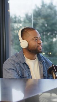 Vertical video: Reacting to offscreen cue host in denim and white headset speaking on mic at desk