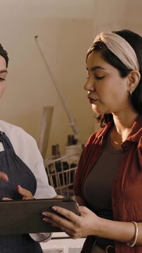 Vertical video: Tapping tablet, chef, manager checking orders at bakery rack with list, in uniform