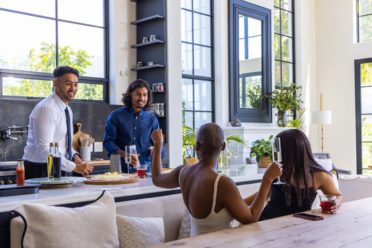Diverse friends chatting around modern home kitchen island, holding wine glasses and phone nearby