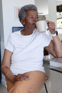 Senior African American woman sipping from beige mug at kitchen counter, smartwatch on wrist
