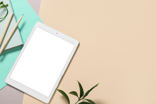 Modern tablet computer with blank screen, pencils and ruscus leaves on color background