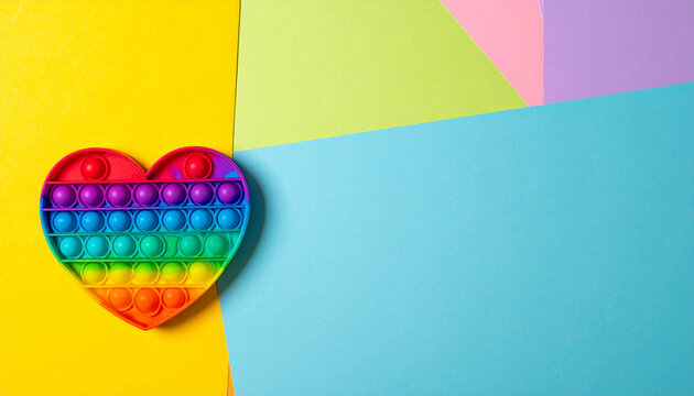 Heart-shaped Pop It Fidget Toy: A vibrant, rainbow-colored heart-shaped pop it fidget toy rests on a colorful, abstract background, symbolizing joy and sensory play.