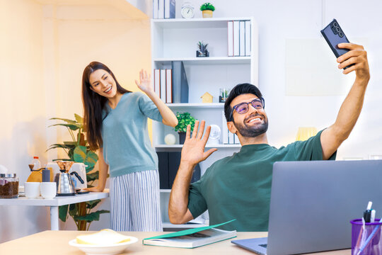 Business couple working, communicating and selfie while sitting at the home office desk together. Cheerful couple, calm asian woman and caucasian man selfi working at home with laptop together.