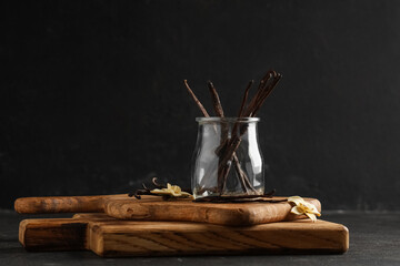 Obraz premium Glass jar with aromatic vanilla sticks and flowers on black grunge background